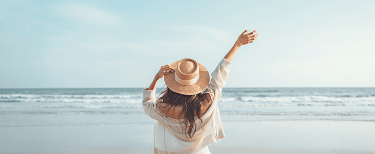 A woman holds her hat and feels the breeze on the beach